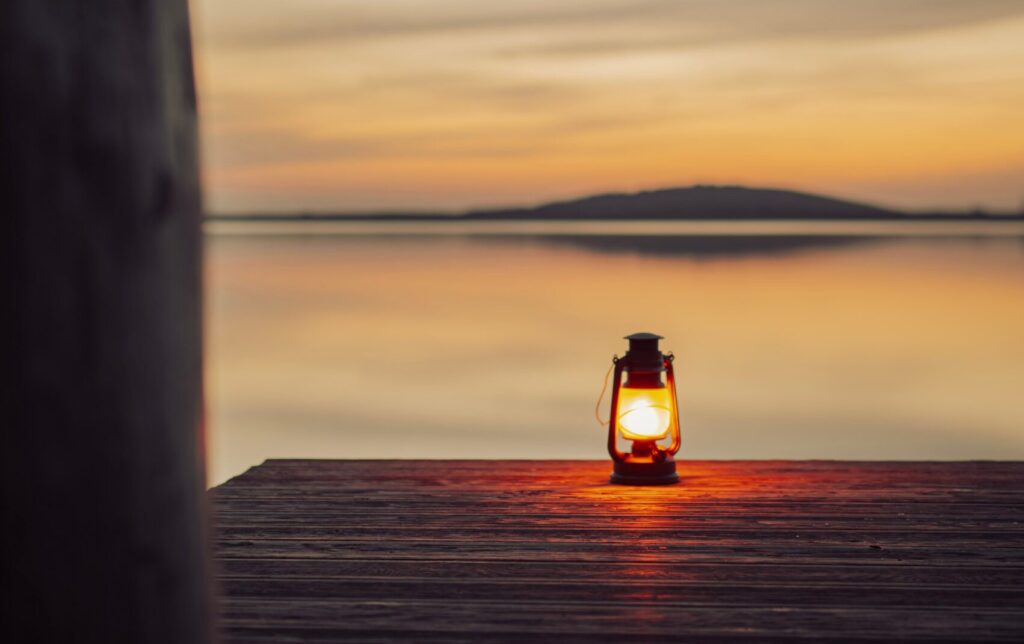 Light at Dusk: A glowing lantern on a wooden pier by a tranquil lake at sunset.