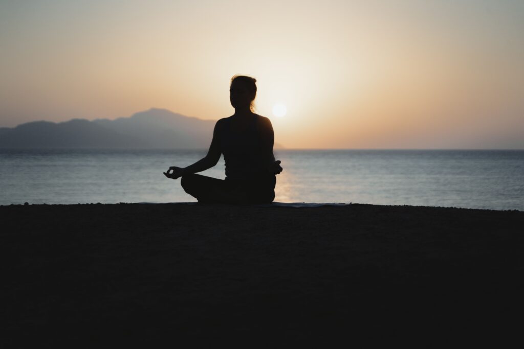 Silhouette of a person meditating in the lotus position on the beach facing the ocean at sunset